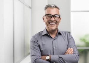 Confident businessman posing in the office with arms crossed, he is smiling at camera